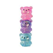 A box of Squeakers 'Sugar Squishy Bears' alongside three translucent glittery bear squishies stacked vertically in pink, purple, and light blue on a white background.