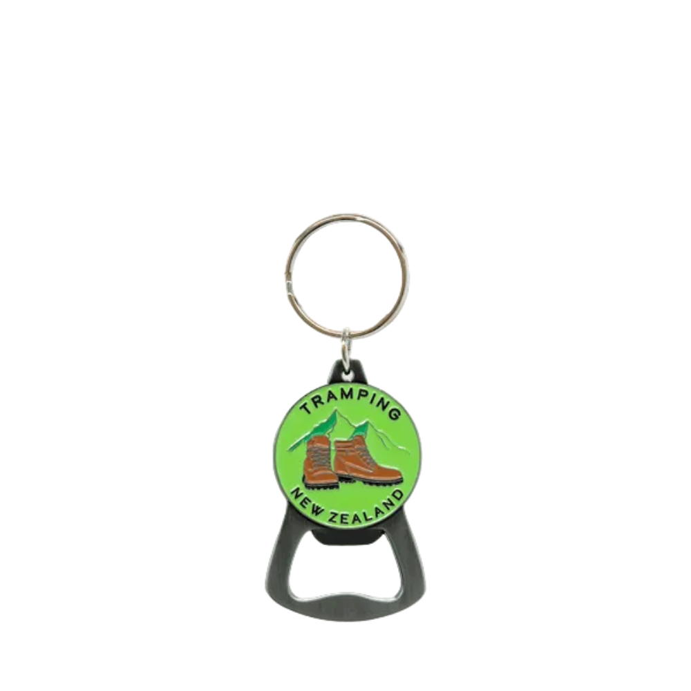 A metal bottle opener keychain with a circular green charm featuring the words 'TRAMPING NEW ZEALAND' and an illustration of hiking boots and mountains, on a light gray background.