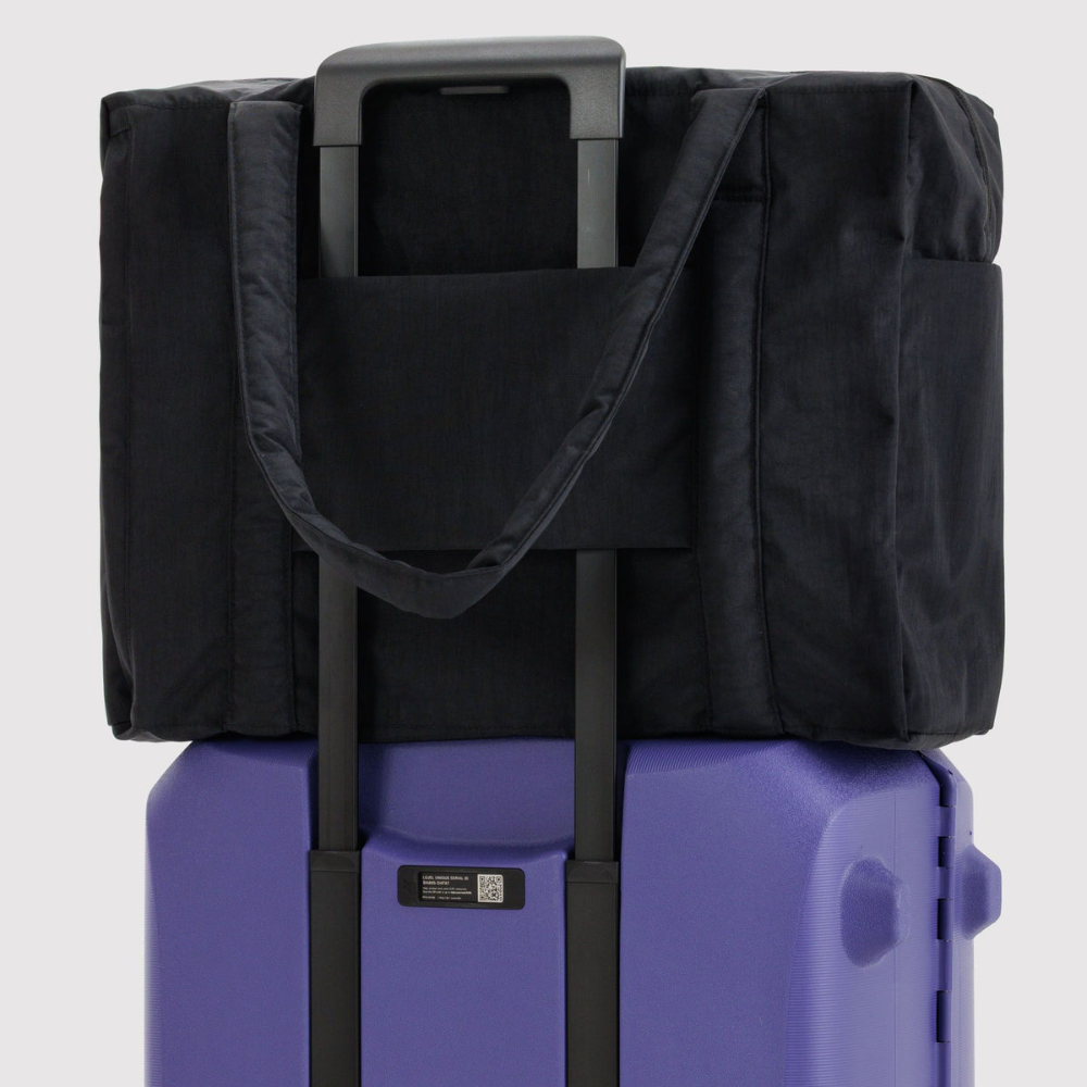 Black bag with handles on a purple suitcase against a white background