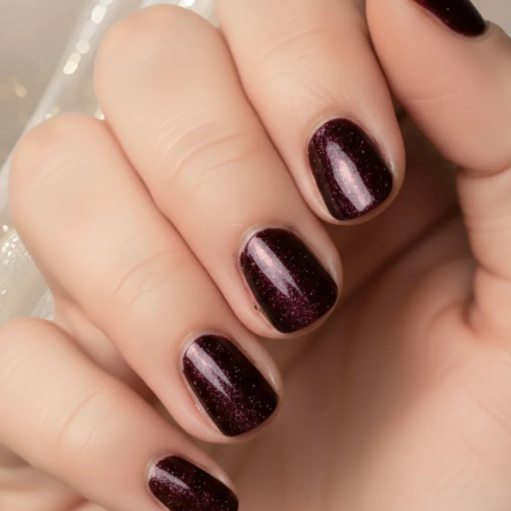 A close-up of a hand with manicured nails painted in a deep glittery burgundy polish.