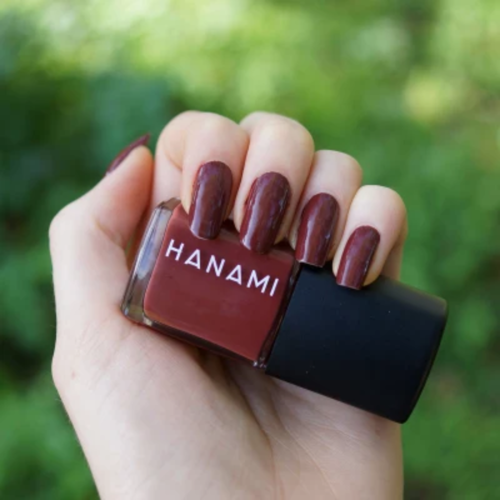 Hand holding a bottle of Hanami nail polish with matching nails against a blurred green background
