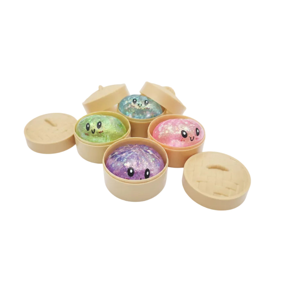 Six small round tan containers with lids, each holding a glittery, iridescent oval charm with a simple black-and-white face. The charms show different colors including green, blue, pink, and purple, and the containers resemble mini steamed dumpling or bento-style boxes.