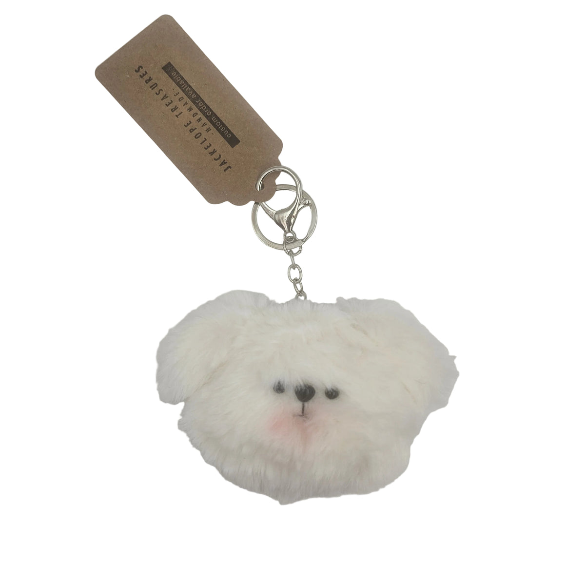 A fluffy white dog-shaped keychain charm with a small pink nose and black eyes, attached to a silver clasp with a brown paper tag that reads 'JACQUEMUS PERPETUAL'.