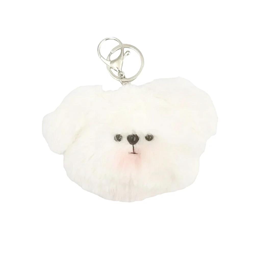 A fluffy white faux-fur keychain shaped like a small dog face, with black embroidered eyes and nose and a pink stitched blush, attached to silver metal key rings on a plain light background.