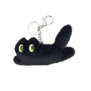 A black plush cat keychain with bright lime green eyes and a silver split ring, attached to a brown paper hangtag that reads 'JASPEUDE TRASHES'.