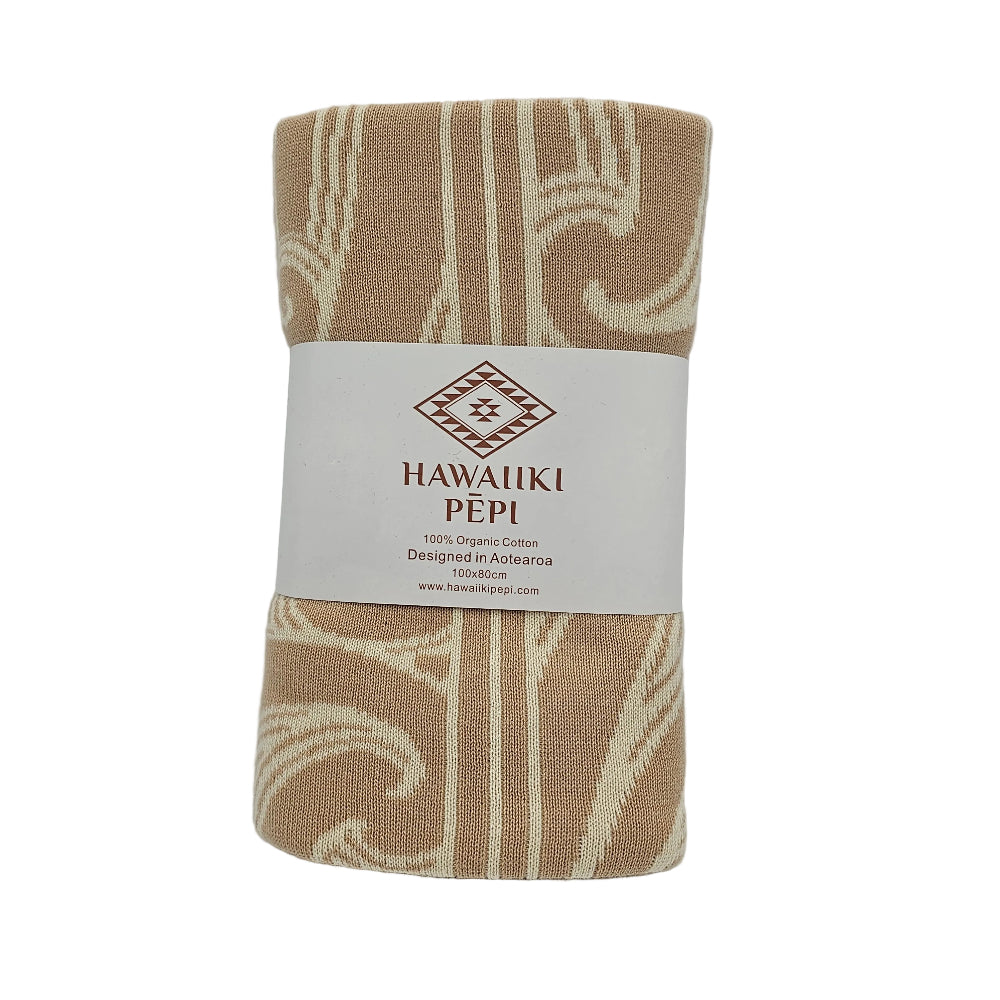 A rolled Hawaiian cotton baby blanket with a beige and cream ikat pattern, wrapped in a white paper band featuring the brand 'HAWAIIKI PEPI'.