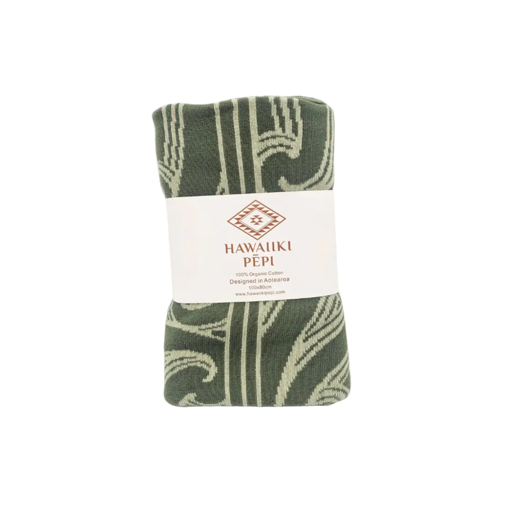 A folded green and cream patterned towel wrapped with a white paper label that reads 'HAWAIIKI PÉPI'.