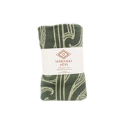 A folded green and cream patterned towel wrapped with a white paper label that reads 'HAWAIIKI PÉPI'.