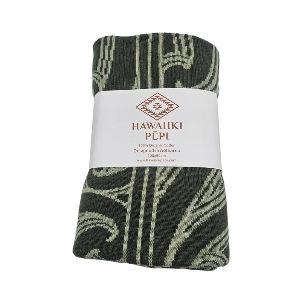 A folded cotton textile with a dark green and light beige ikat-style pattern, wrapped in a white paper band labeled HAWAIIKI PEPI.