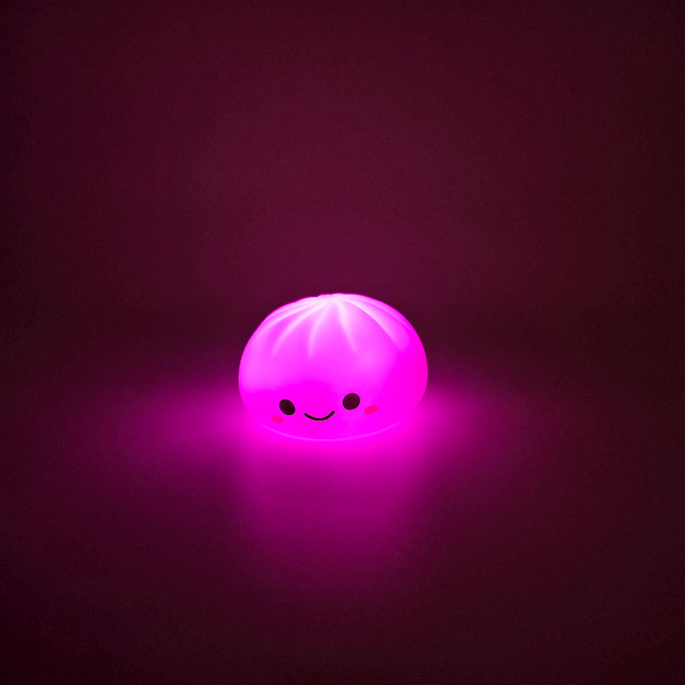 A cute, round, dumpling-shaped glowing night light with a smiling face, emitting a bright pink light against a dark background.