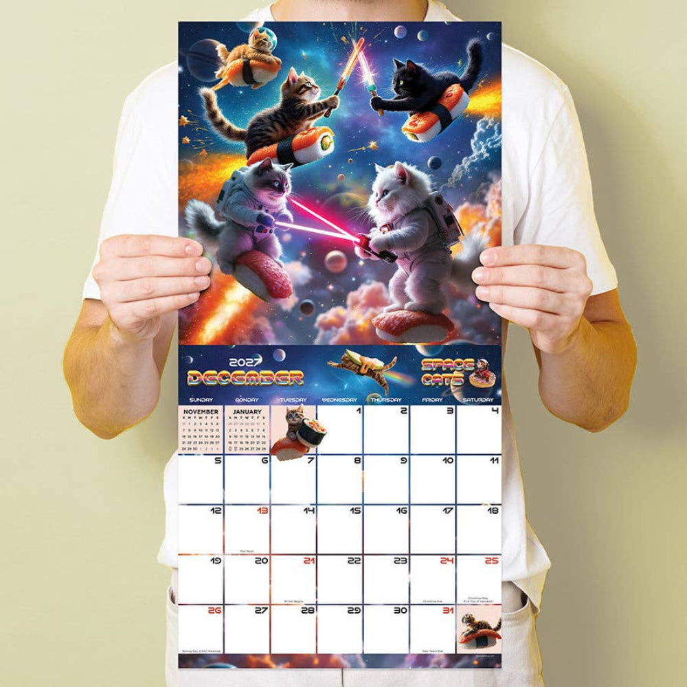 A person in a white t-shirt holds up a December 2022 calendar page featuring a colorful cartoon space scene with cats and dogs in space suits, with the rest of the calendar grid visible below.