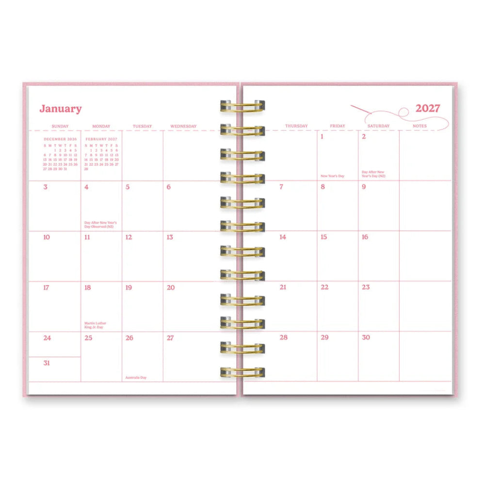 An open 2027 ring-bound planner showing the January and 1st weekly spreads, featuring a light pink cover and gold metal rings.