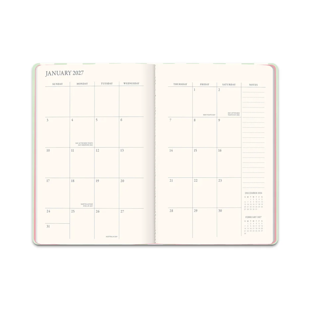 An open planner or journal showing the January 2027 page spread, with cream-colored interior pages, black printed calendar grids, and a thin pastel multicolor border visible along the outer edges, photographed on a plain white background.