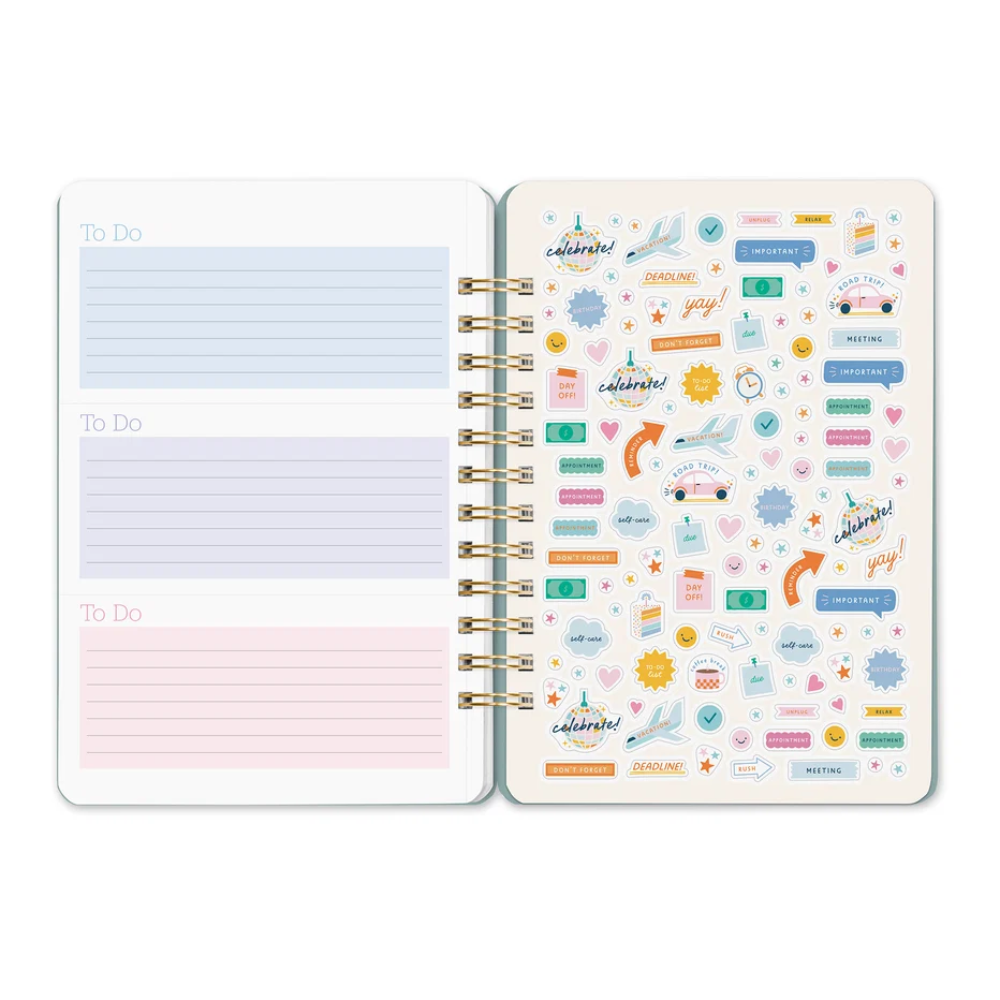 An open spiral-bound planner or notebook showing two decorated pages. The left page has three light blue and pink lined 'To Do' sections, and the right page is covered in colorful decorative stickers including airplanes, maps, calendar icons, and motivational phrases.