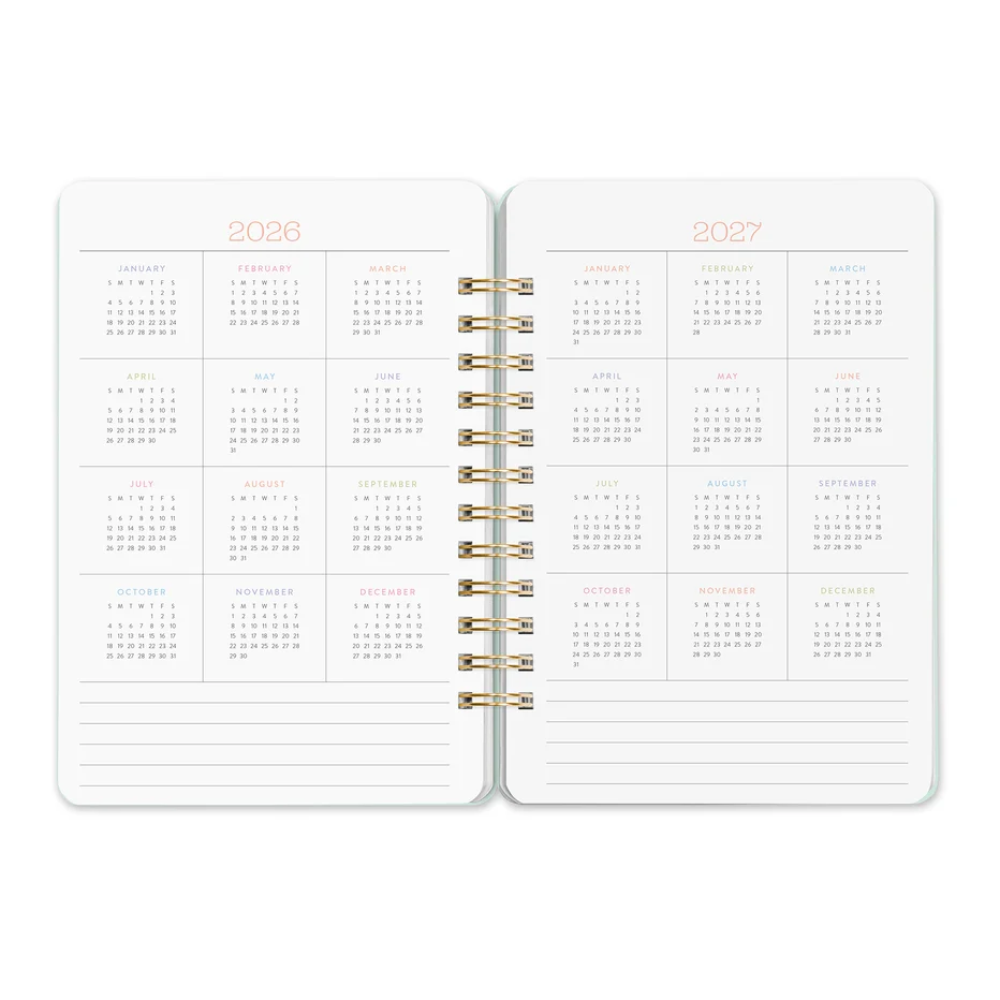 An open spiral-bound planner showing the interior calendar spreads for 2026 and 2027, with monthly grids and lined writing sections on white pages.