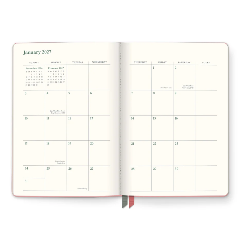 An open planner or journal showing the January 2027 calendar spread, with cream pages, thin blue grid lines, and two small ribbon bookmarks at the bottom. The product is photographed on a clean white background.