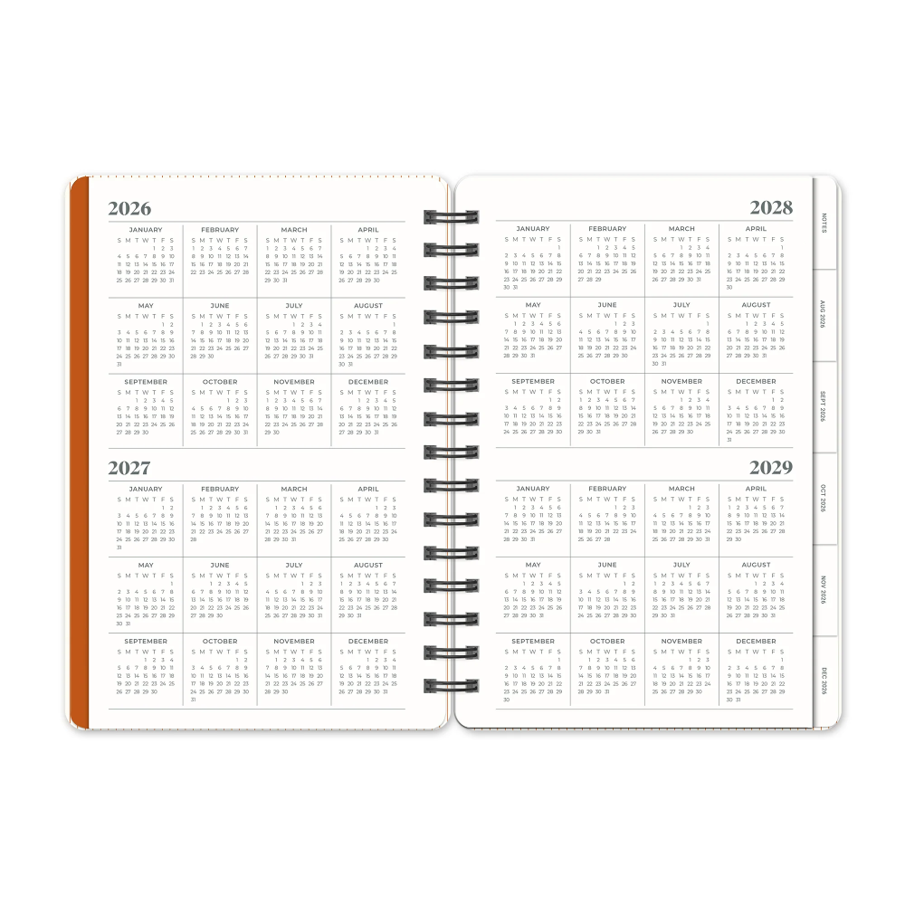 An open spiral-bound planner or calendar showing the years 2026 through 2029 on the inner pages, with a white cover and a narrow orange accent strip on the left edge, photographed on a plain white background.