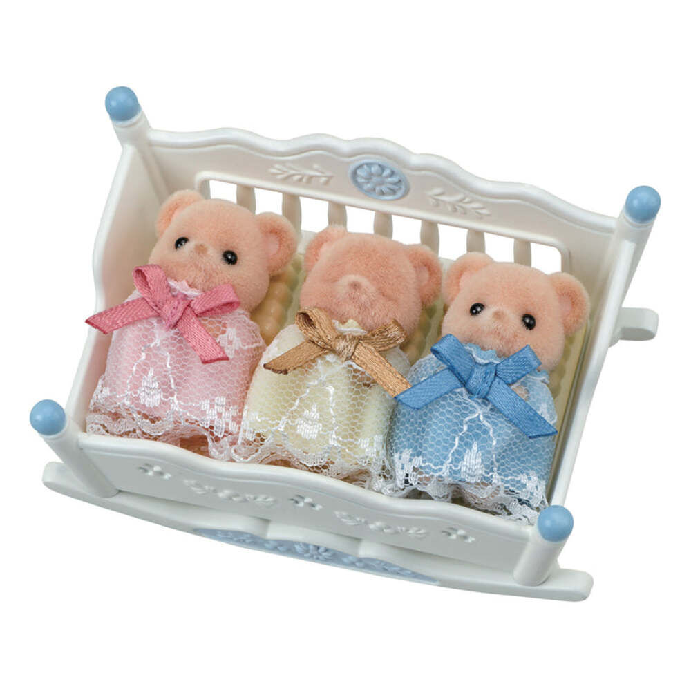 Three teddy bears in dresses sitting in a white crib on a white background