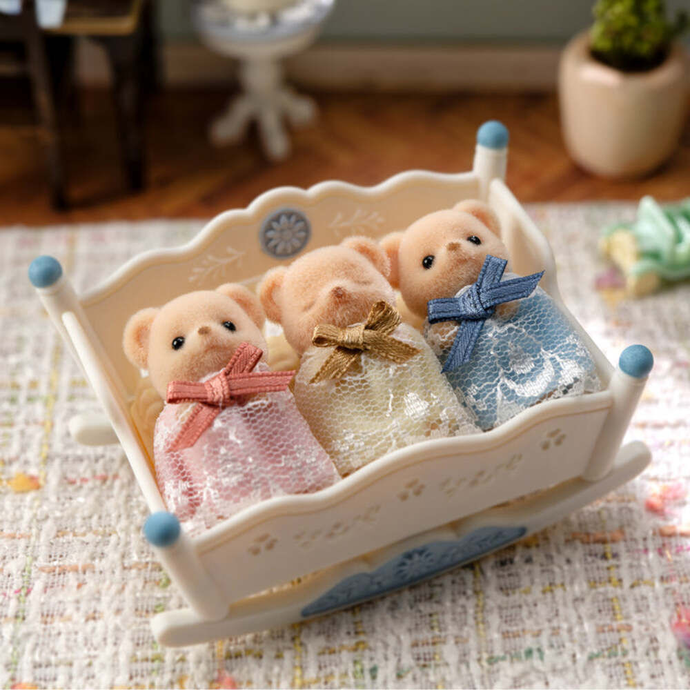Three teddy bears in a decorative crib with colorful ribbons on a patterned surface.