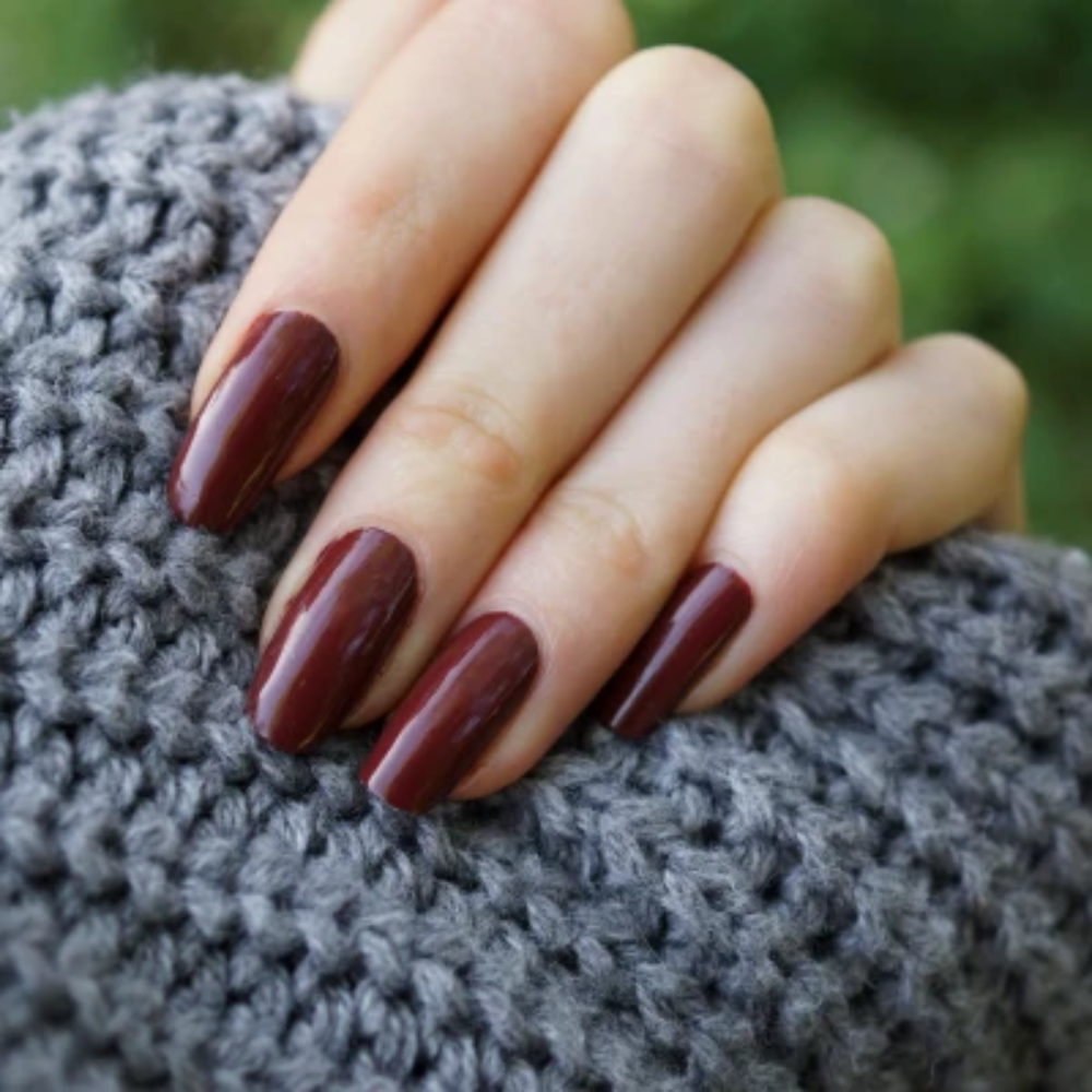 Close-up of a hand with dark red nail polish on a textured gray surface.