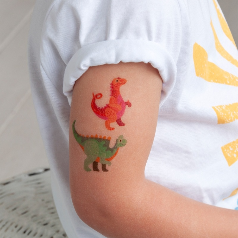 A child wearing a white t-shirt with a colorful temporary tattoo of two cartoon dinosaurs on their upper arm.