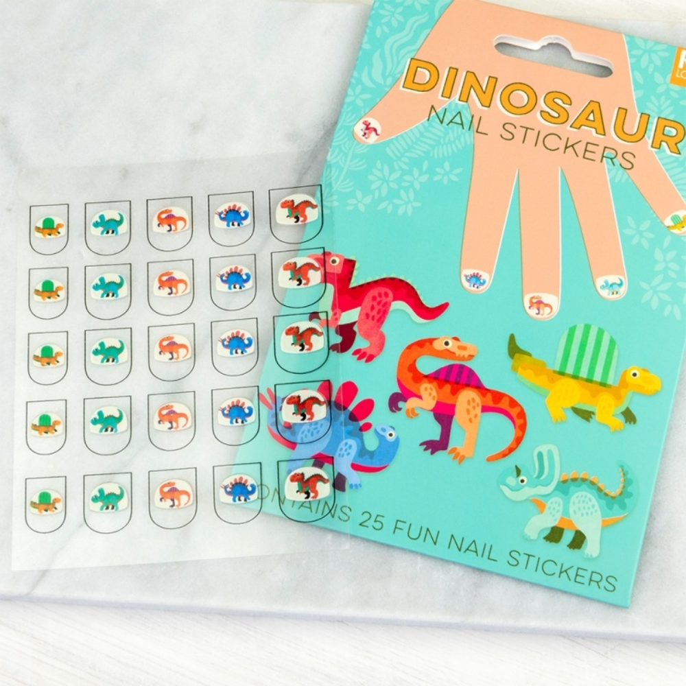 A package of dinosaur nail stickers shown next to a sheet of individual nail stickers on a light marble surface. The packaging is teal with a large hand illustration and colorful cartoon dinosaurs, while the sheet contains small oval stickers with different dinosaur designs.