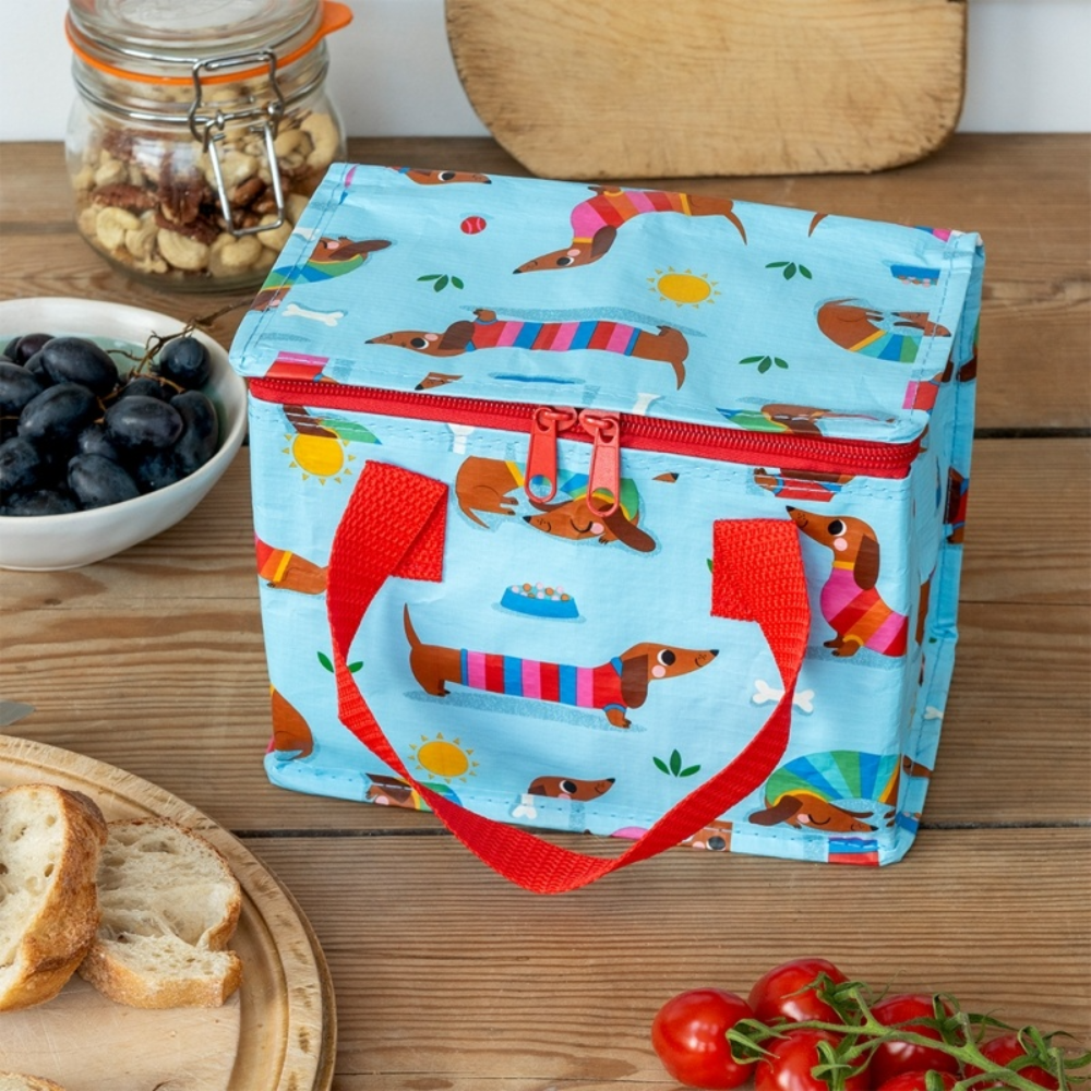 Colorful lunch bag with dachshund pattern on a wooden table with food items.