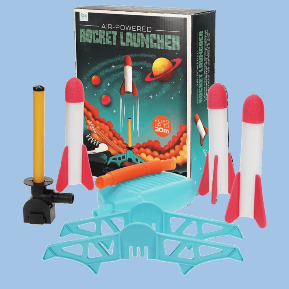 An air-powered toy rocket launcher set with a black and green box, a blue launching platform, three white rockets with red fins, a yellow and black pump, and orange nozzles, arranged on a white background.