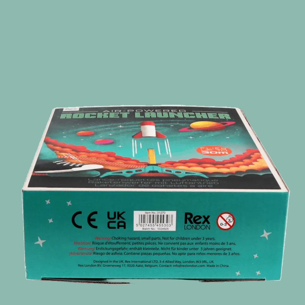 The product packaging box for the 'Rocket Launcher' toy, featuring a teal base with a colorful illustration of a rocket launching into space with planets and stars. The back of the box displays regulatory compliance logos (CE, UKCA), a barcode, and the brand 'Rex London'.