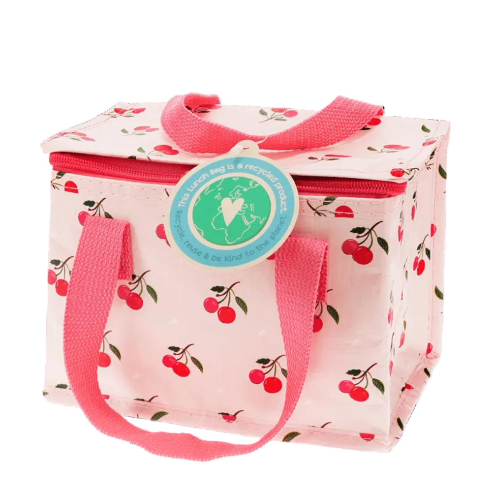 A pink insulated lunch bag with a cherry print pattern, featuring pink handles and a round blue and green 'The Lunch Bag is a recycled product' sticker on the front, set against a plain white background.