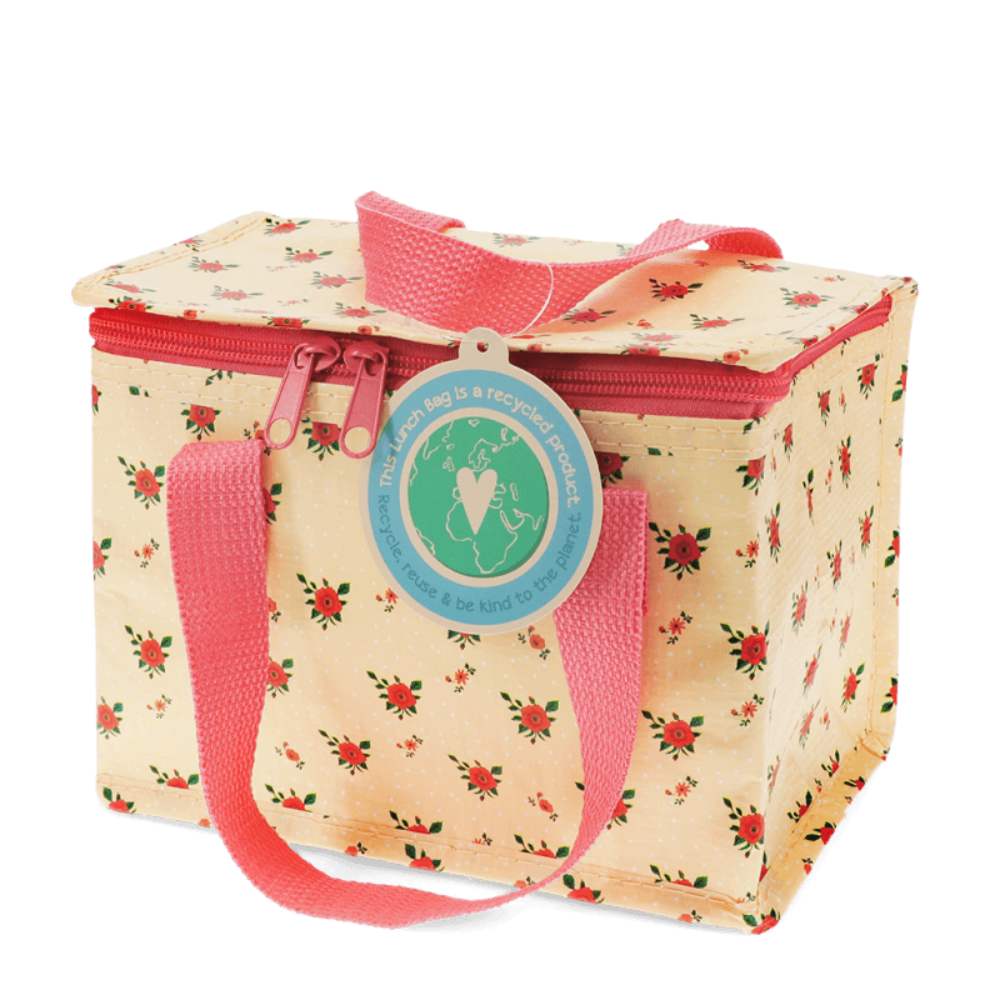 A square reusable lunch bag with a cream background, red and green floral print, pink handles, and a circular hanging tag that reads 'The lunch bag is a recycled product. You can use it, be kind to it, and pass it on.