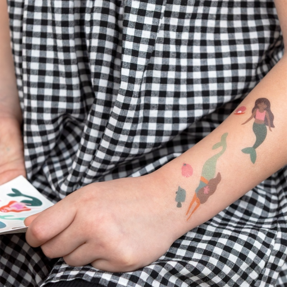 Person with temporary tattoos of mermaids on a checkered fabric background