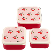 Three square lunch boxes with red bodies and light pink lids decorated with a cherry print, arranged on a white background.