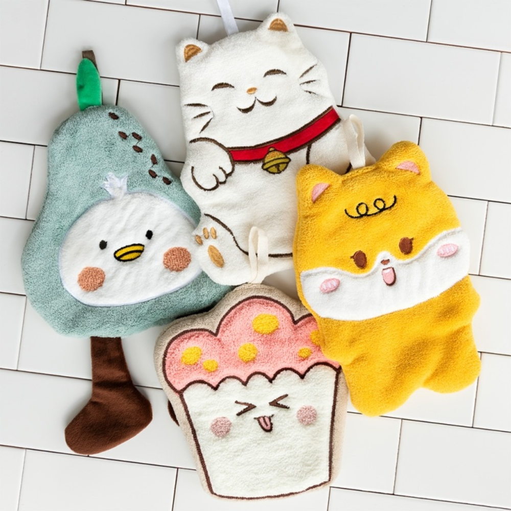 Four plush character bath towels laid out on a white tiled floor: a pear-shaped duck character, a white cat with a red collar, a yellow cat character, and a cupcake character.