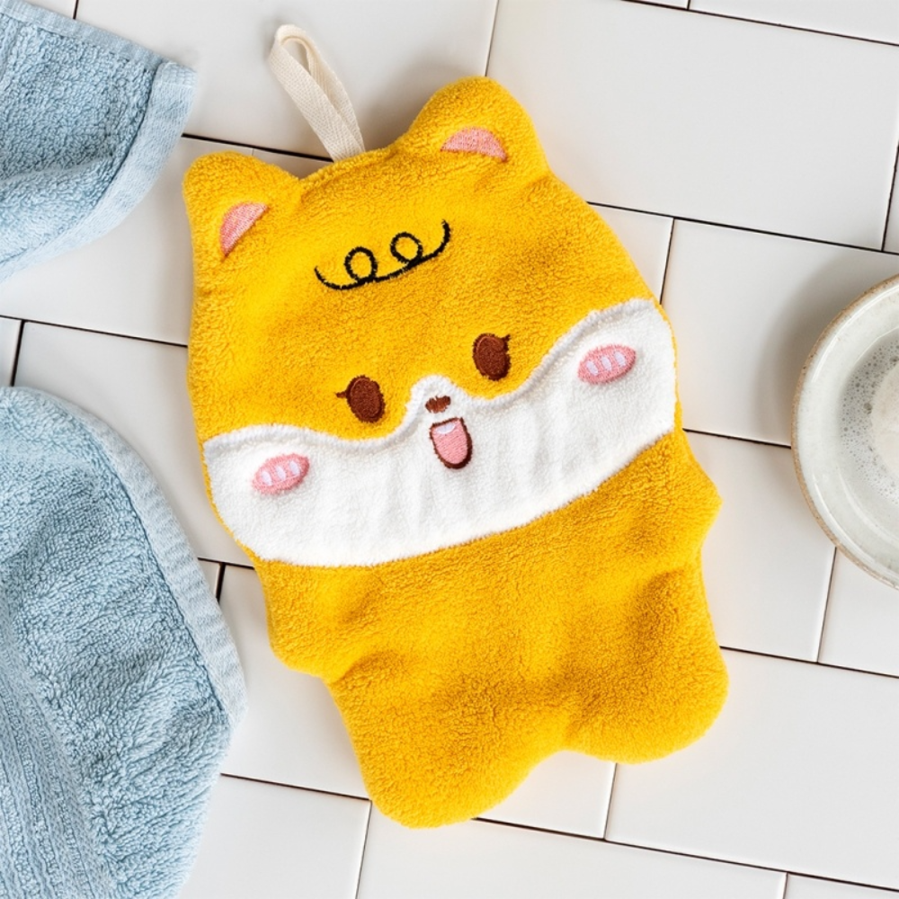 A yellow plush dog-shaped hand towel with a white snout and embroidered face details, laid flat on a white tiled surface next to a blue towel.