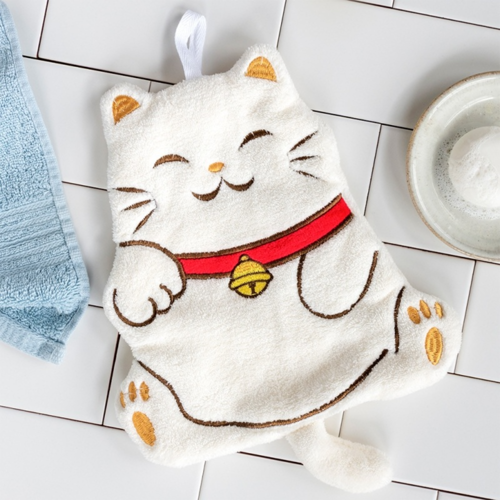 White towel shaped like a cat with a red collar and yellow bell on a tiled floor.