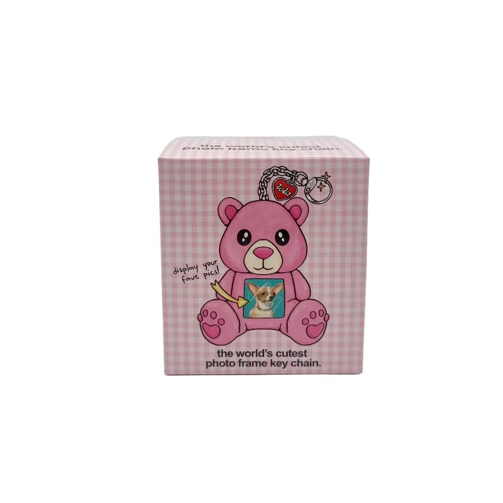 A pink gingham box featuring a cartoon pink bear holding a photo frame keychain, photographed against a plain light gray background.