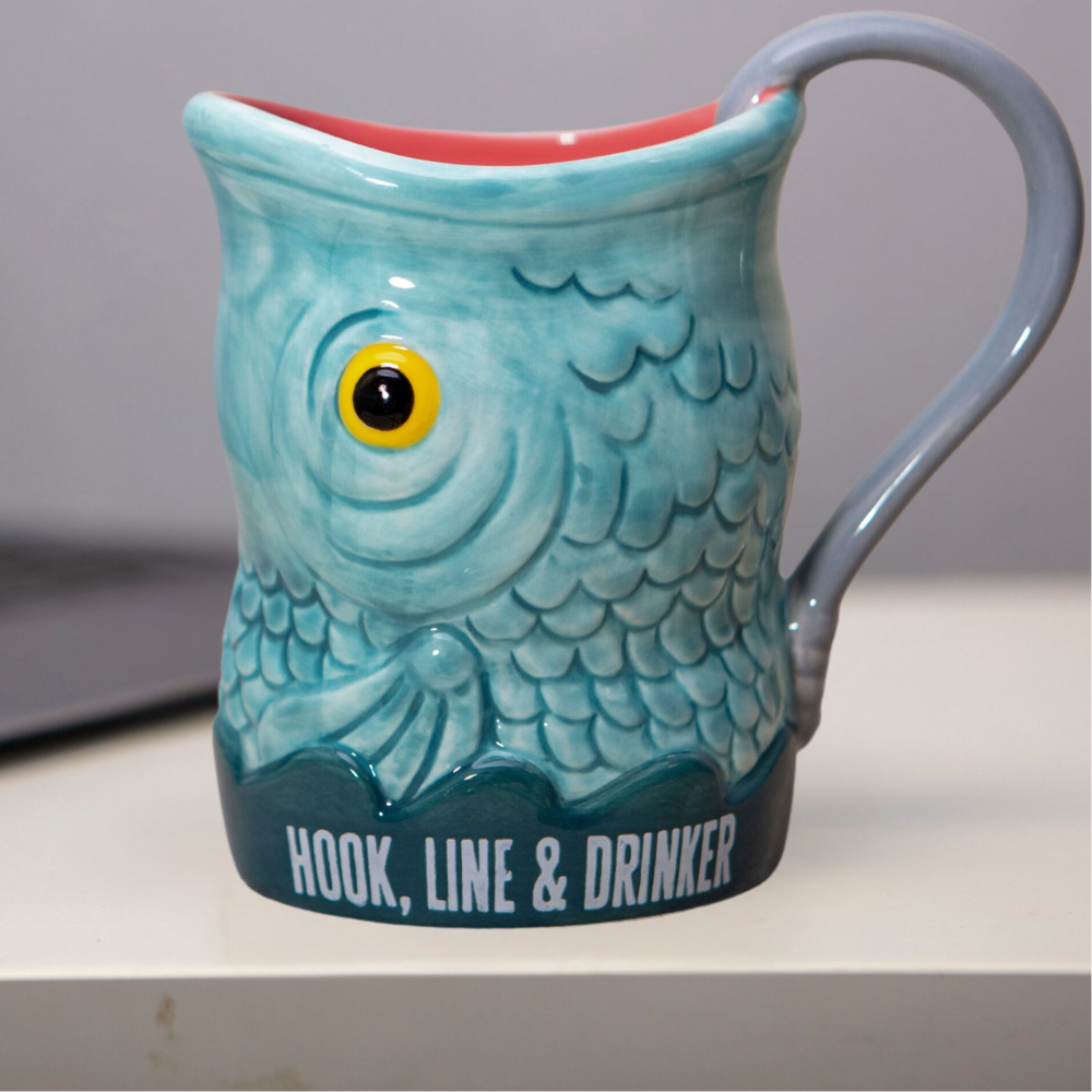 Fish-shaped mug with 'Hook, Line & Drinker' text on a desk.