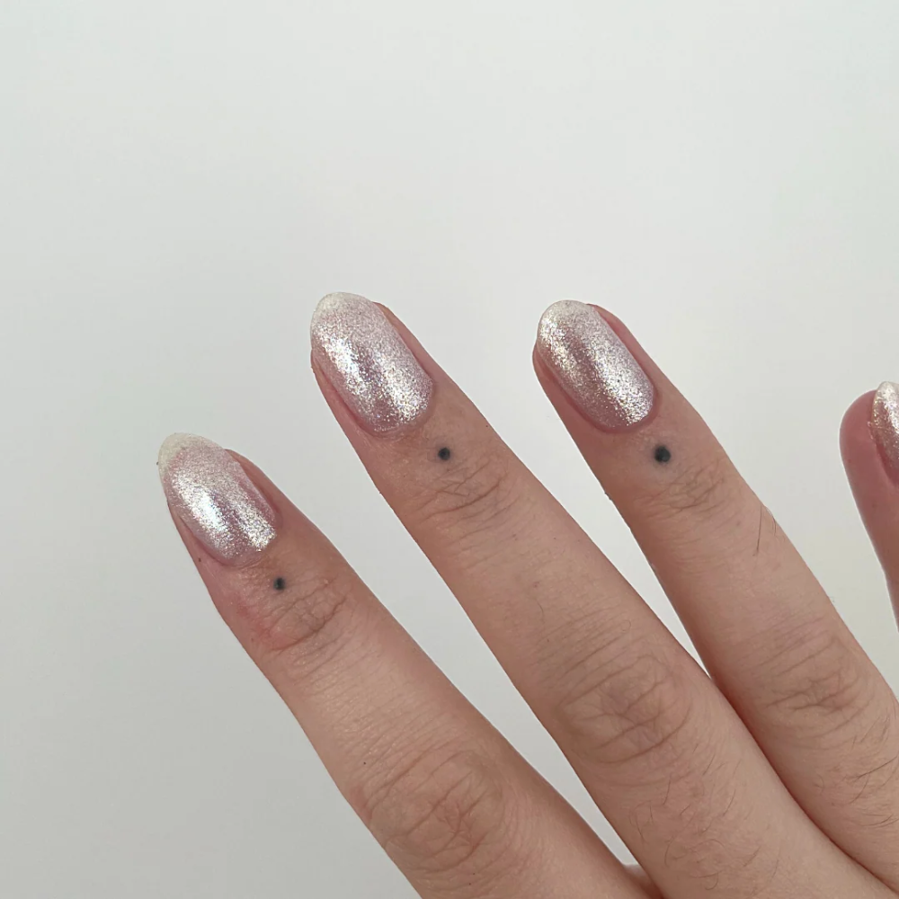 Close-up of a hand with glittery silver nail polish on a plain background