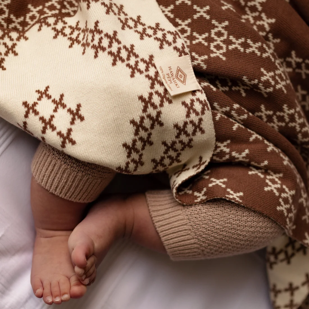 Baby's legs in brown and beige patterned pants on a white surface