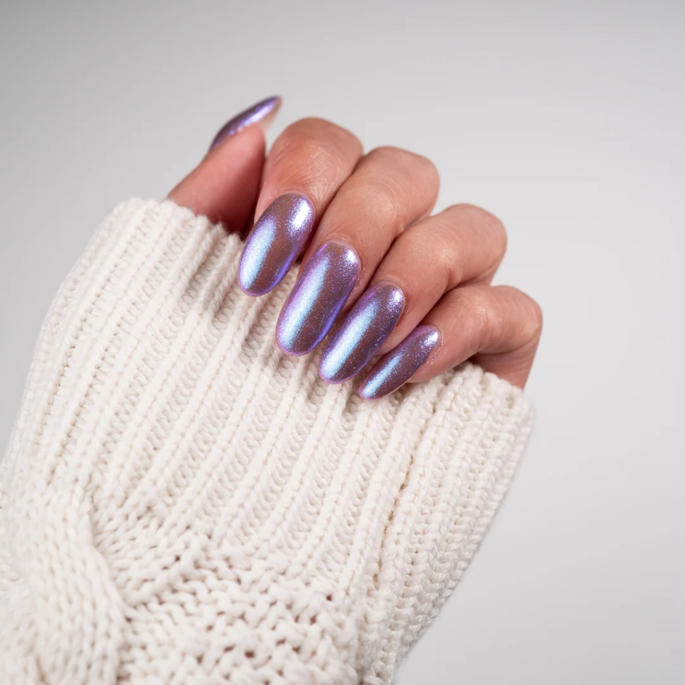 A close-up of a hand wearing a chunky cream knit glove, showcasing manicured nails with a metallic, holographic lavender-purple chrome finish.