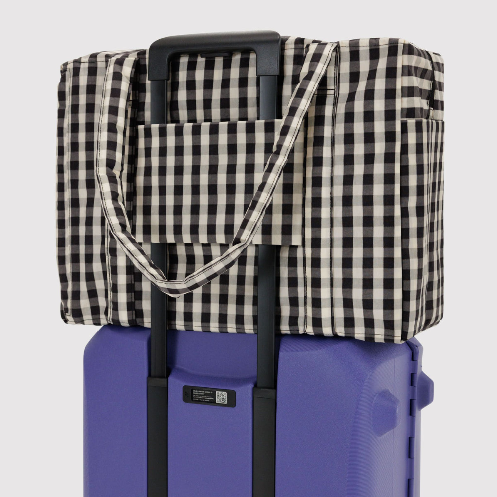Checkered bag draped over a purple suitcase on a light gray background