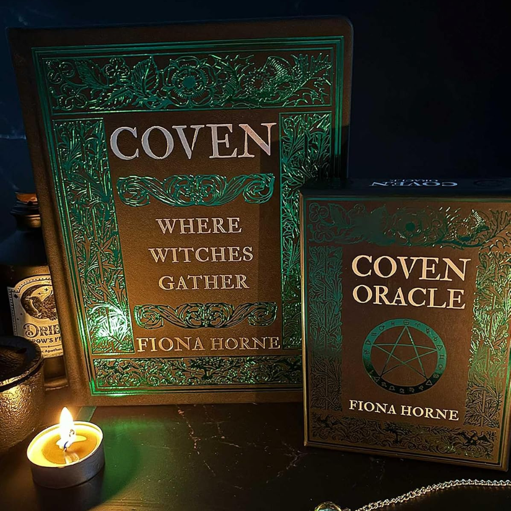 Two books titled 'Coven' and 'Coven Oracle' by Fiona Horne on a dark surface with a lit candle.