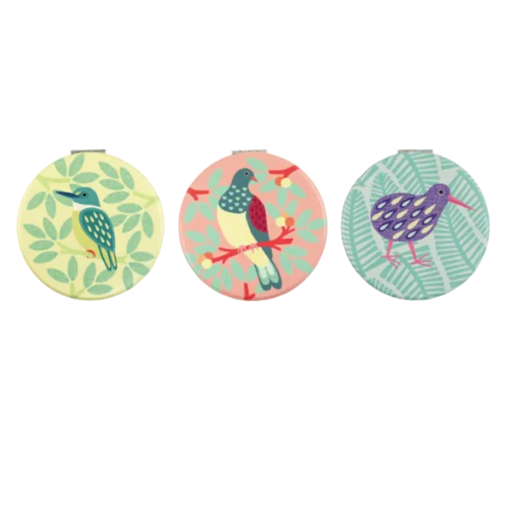 A display box of New Zealand cosmetic mirrors with three round mirrors shown above and inside the open box. The mirrors feature colorful tropical bird designs on pastel backgrounds, including a green kingfisher, a pink-and-blue toucan, and a purple kiwi.