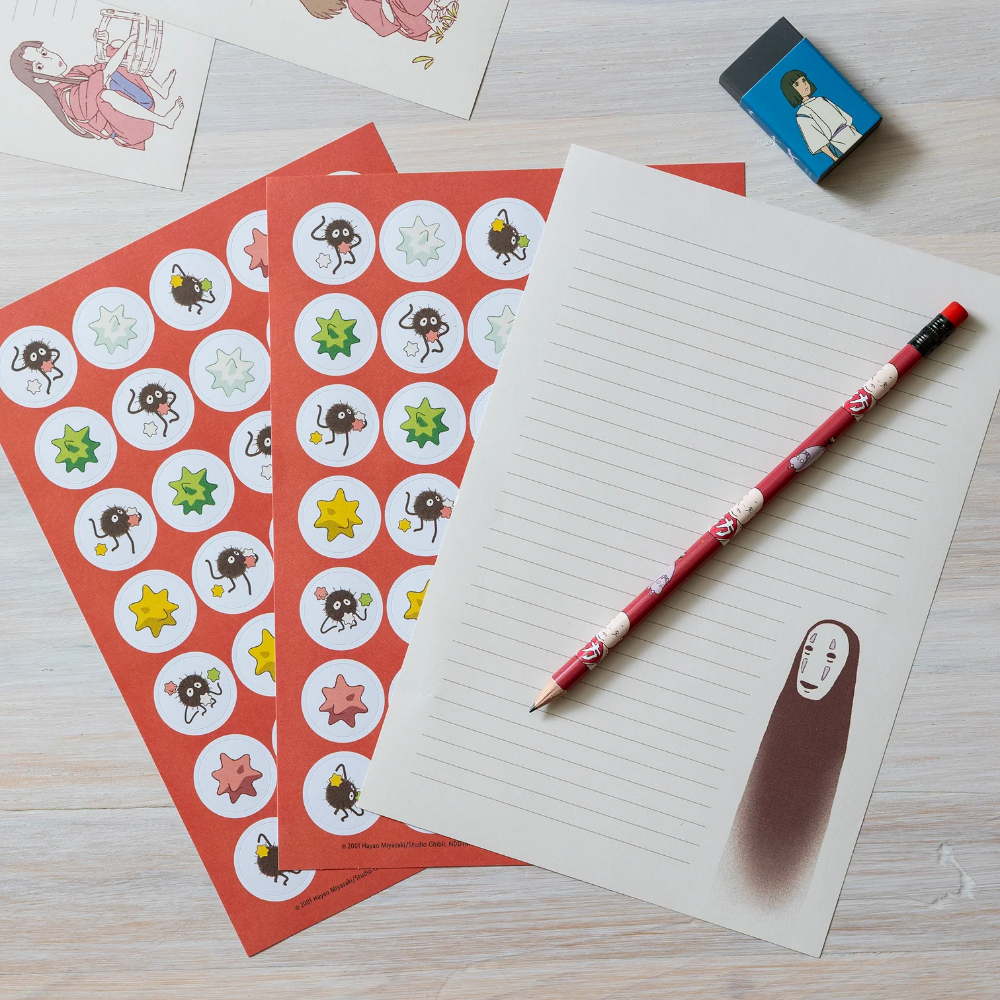 A styled flat-lay of a notebook with lined pages and a matching red pencil, alongside red sticker sheets featuring cartoon characters and stars, on a light wood surface.