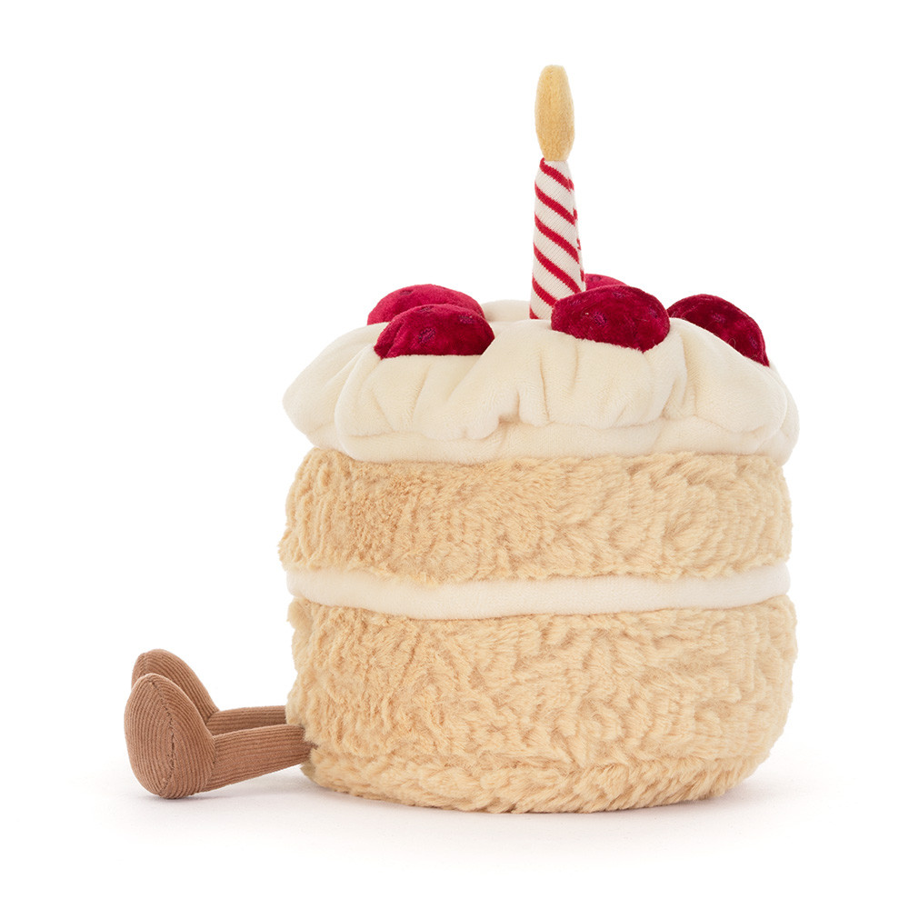 A plush birthday cake toy with textured cream-colored frosting, red velvet-like cherries, and a single red-and-white striped candle, shown on a plain white background.