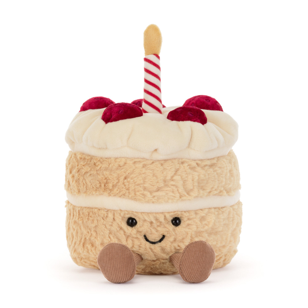 A plush cake toy with cream-colored frosting, red cherries, a red-and-white striped candle, and a smiling face on a white background.