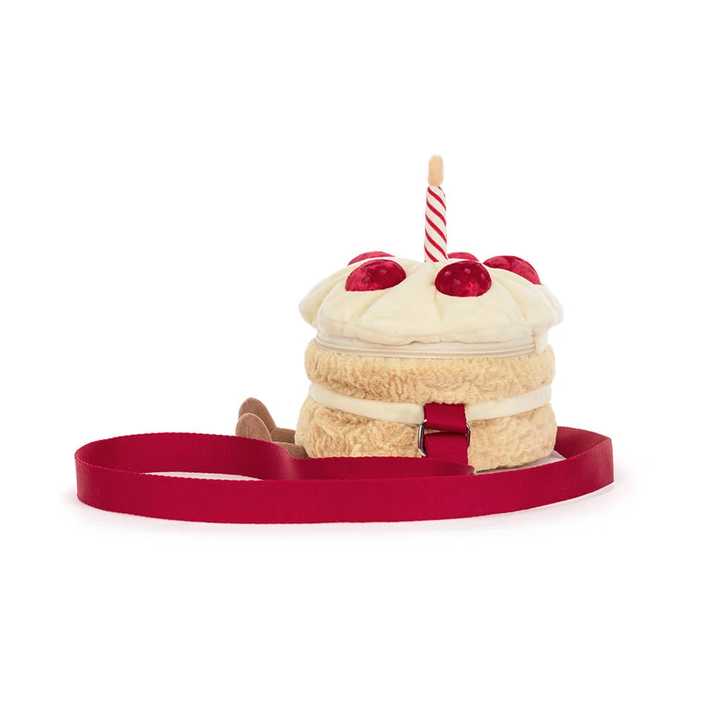 A plush cake-shaped bag with cream-colored frosting, red cherry details, a striped candle, and a red strap, shown on a plain white background.