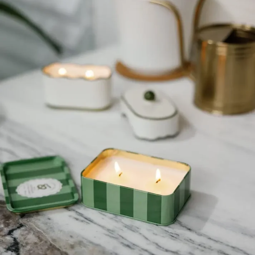 Green striped candle in a tin on a marble surface with blurred background