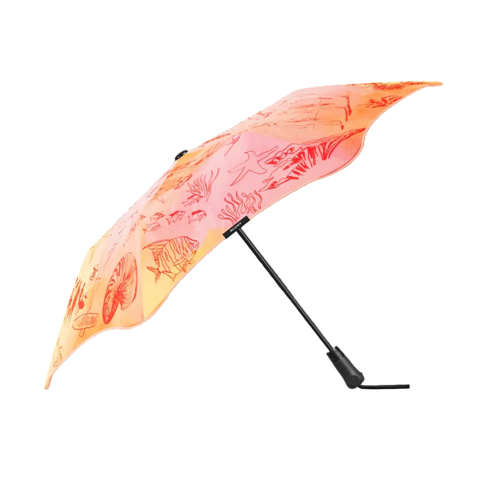 A compact folding umbrella with a scalloped edge, featuring a vibrant orange and pink tropical fish print on the canopy, shown open against a solid white background.
